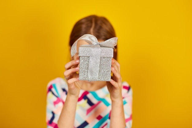 Una linda niña adolescente sostiene una caja de regalo plateada en una mano en el estudio