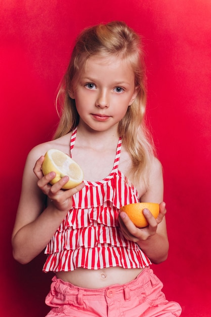 Foto linda niña adorable con frutas sobre fondo rojo.