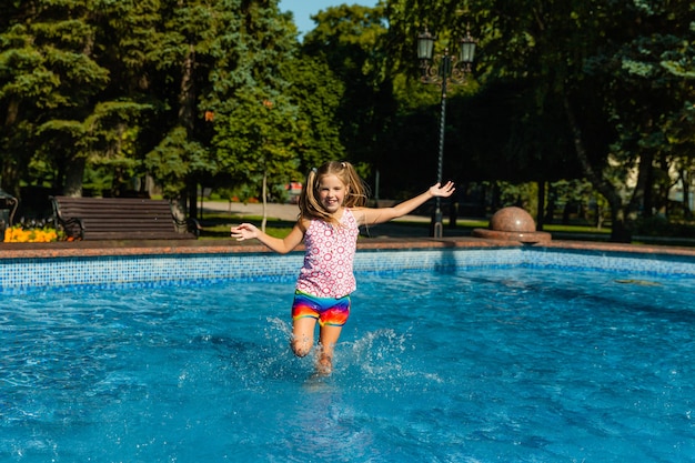 Linda niña alegre está jugando en la fuente. El niño se divierte en un parque de verano en la fuente de la ciudad.