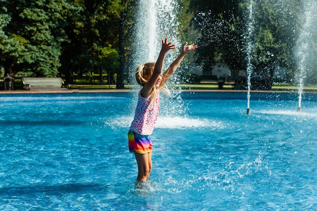 Linda niña alegre está jugando en la fuente. El niño se divierte en un parque de verano en la fuente de la ciudad.