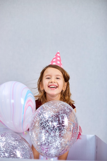 Linda niña alegre con vestido rosa y sombrero juega con globos en casa serpentinas de fiesta de cumpleaños Feliz cumpleaños Celebrando