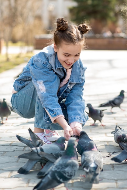 Una linda niña alimenta a las palomas en el parque Niños y animales