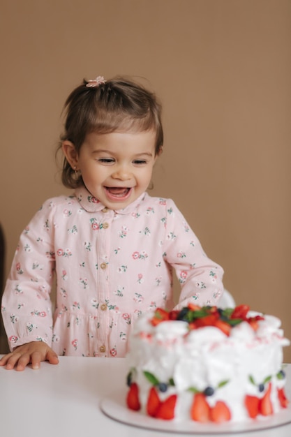 Linda niña de un año y medio junto a un delicioso pastel de cumpleaños Una niña de dieciocho meses muy feliz y se ríe Comida vegetariana Sin lactosa y sin gluten