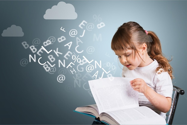 linda niña con anteojos leyendo un libro con letras de salida sobre pizarra