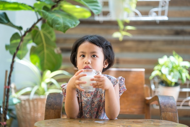 Linda niña asiática bebiendo leche orgánica fresca en el jardín