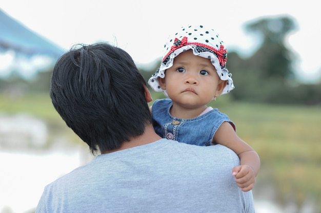 Linda niña asiática en el brazo de su papá con sombrero con lunares.