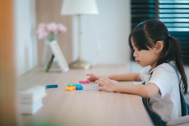 Linda niña asiática disfrutando mientras juega con juguetes o bloques sentados en la mesa