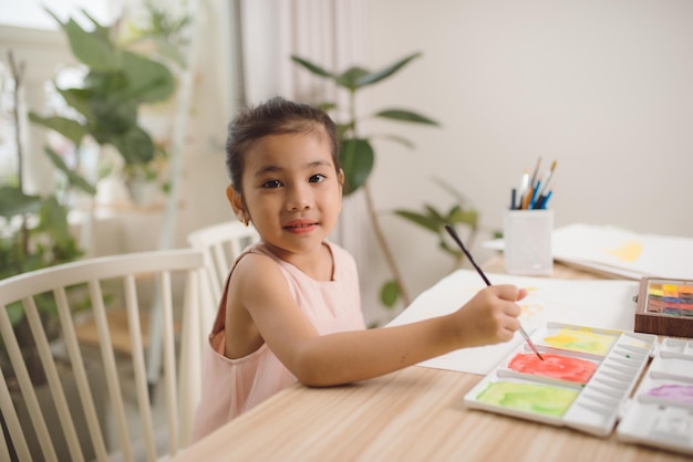 Linda niña asiática disfrutando de pintar en casa con color de agua de papel y pincel de arte