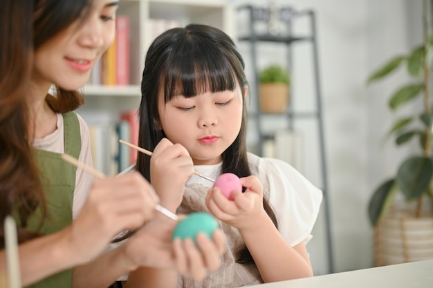 Una linda niña asiática se enfoca en colorear un huevo de Pascua con su mamá