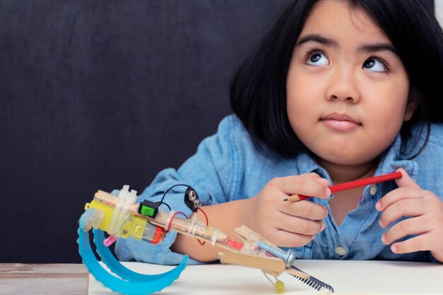 Una linda niña asiática está aprendiendo a ensamblar un robot durante el horario escolar Pensando en comenzar a aprender innovación