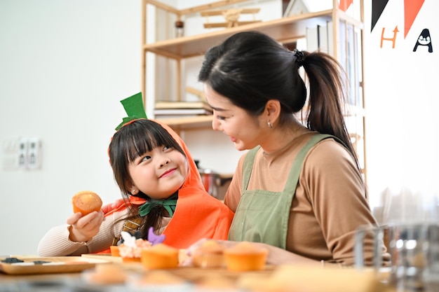 Linda niña asiática feliz de hacer cupcakes de Halloween con su mamá