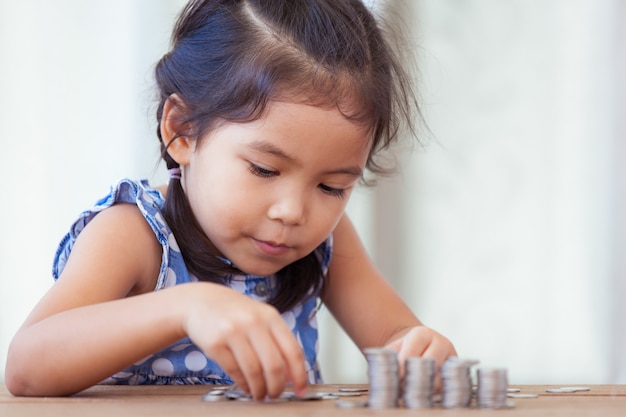 Linda niña asiática haciendo pilas de monedas.