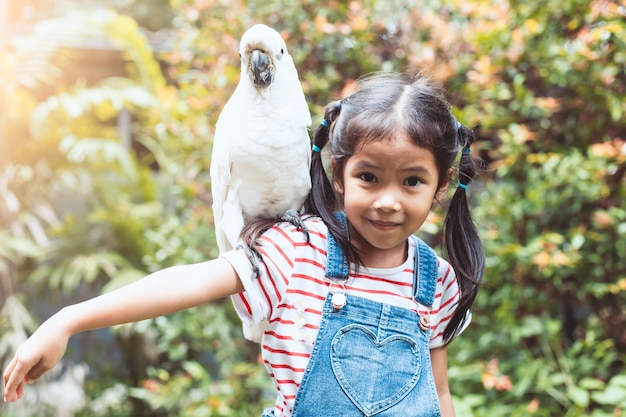 Linda niña asiática con hermoso loro guacamayo en su hombro en el zoológico