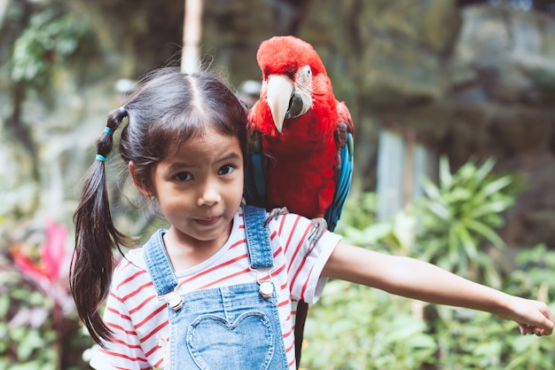 Linda niña asiática con hermoso loro guacamayo en su hombro en el zoológico