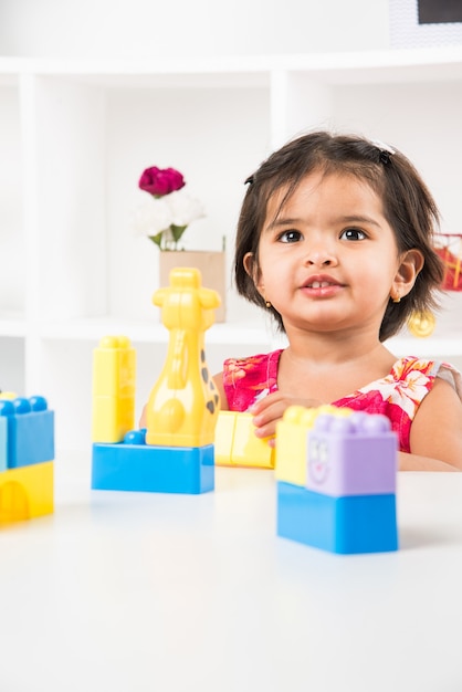 Linda niña asiática india disfrutando mientras juega con juguetes o bloques, sentado en la mesa