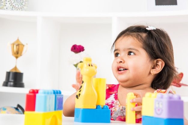 Linda niña asiática india disfrutando mientras juega con juguetes o bloques, sentado en la mesa