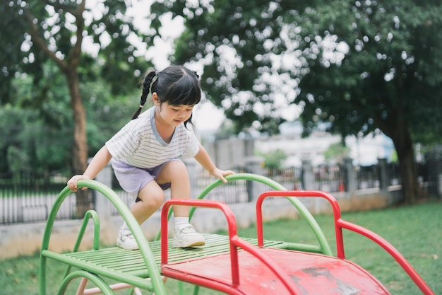 Linda niña asiática juega en la escuela o en el patio de la guardería o en el patio de recreo Actividad de verano saludable para niños Niña asiática escalando al aire libre en el patio de recreo Niño jugando en el patio de recreo al aire libre