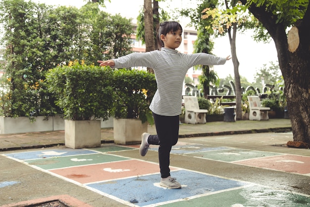 Linda niña asiática jugando a la rayuela al aire libre. Divertido juego de actividades para niños en el patio de recreo al aire libre. Deporte callejero de verano en el patio trasero para niños. Estilo de vida de la infancia feliz.