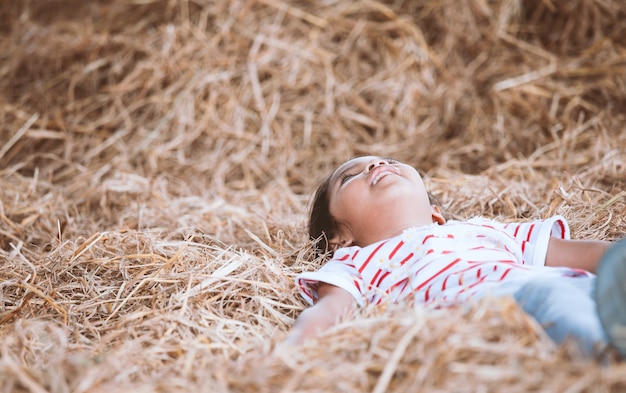 Linda niña asiática niño acostado en el heno y jugar con la pila de heno en la granja