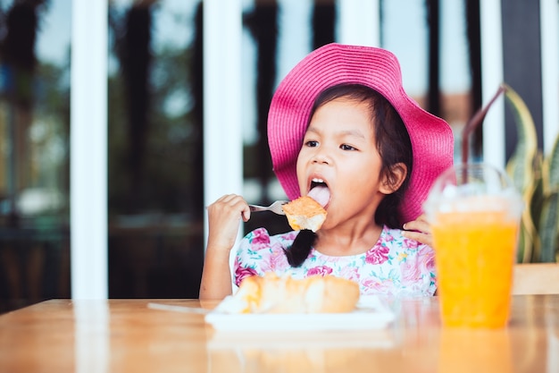 Linda niña asiática niño comiendo deliciosas tostadas y jugo de naranja
