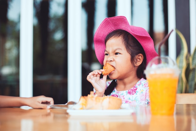 Linda niña asiática niño comiendo deliciosas tostadas y jugo de naranja