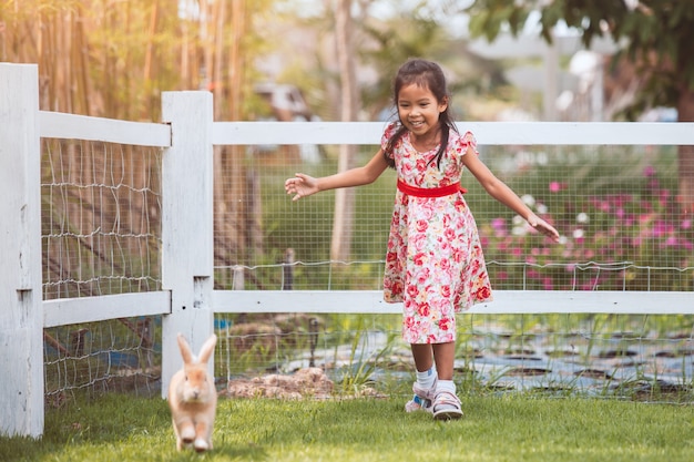Linda niña asiática niño corriendo para atrapar un conejo con diversión en el jardín