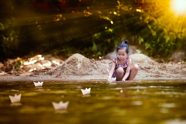 Linda niña asiática niño jugando bote de papel en la orilla del río en verano