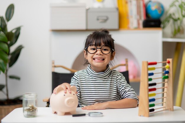 Linda niña asiática poniendo dinero en la alcancía para ahorrar dinero para el futuro