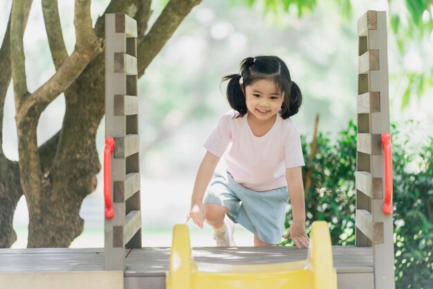 Linda niña asiática sonríe escalando escaleras y juega en la escuela o en el patio de la guardería o en el patio de recreo Actividad de verano saludable para niños Niña asiática divertida feliz Niño jugando en el patio de recreo al aire libre