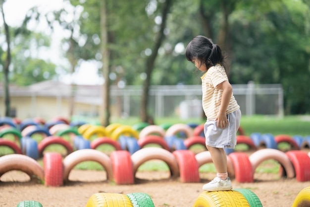 Linda niña asiática sonríe y juega en la escuela o en el patio de la guardería o en el patio de recreo Actividad de verano saludable para niños Niña asiática escalando al aire libre en el patio de recreo Niño jugando en el patio de recreo al aire libre