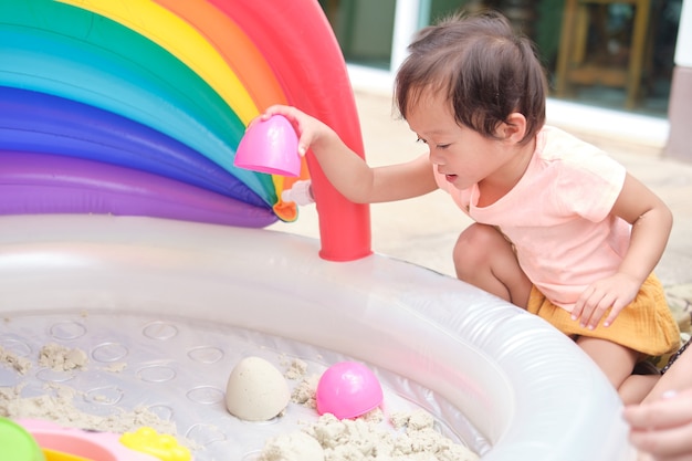 Foto linda niña asiática sonriente de 2 años de edad, niño jugando con arena cinética en el arenero en casa