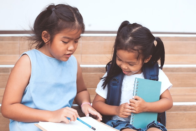 Linda niña asiática y su hermana leyendo un libro juntos