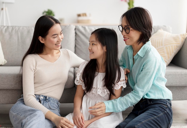 Linda niña asiática con su madre y su abuela mirándose sentadas en el suelo en la vida