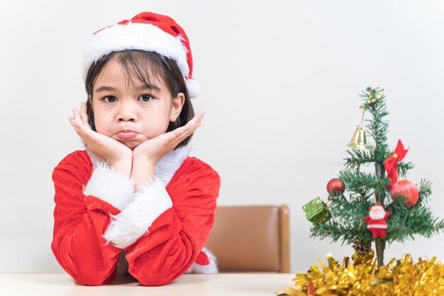 Una linda niña asiática en un vestido rojo de Santa Claus decorando el árbol de Navidad en la víspera de Navidad