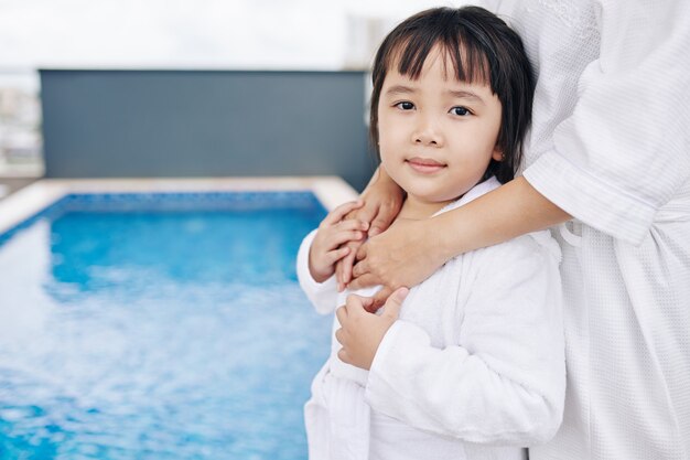 Linda niña asiática vistiendo bata de baño blanca después de nadar en la piscina