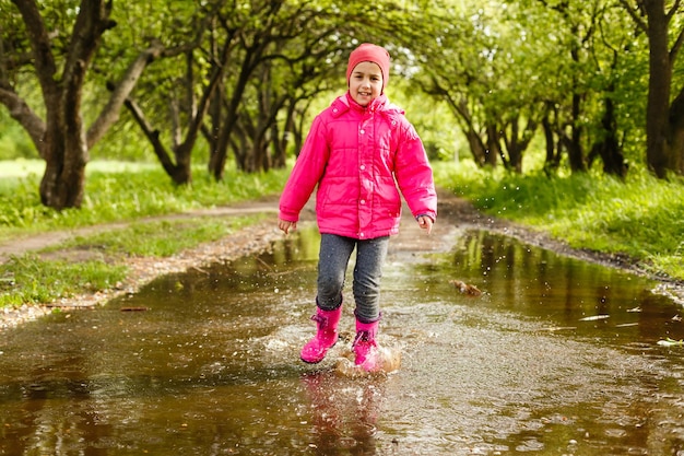 linda niña con botas de lluvia saltando a un charco