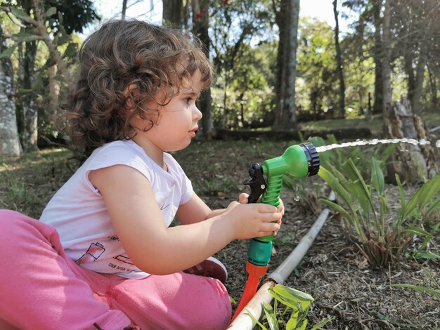 Linda niña brasileña divirtiéndose jugando con manguera de agua en el jardín.