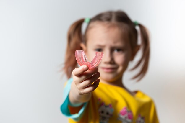 Linda niña con cabello rubio sostiene un entrenador miofuncional dental rosa