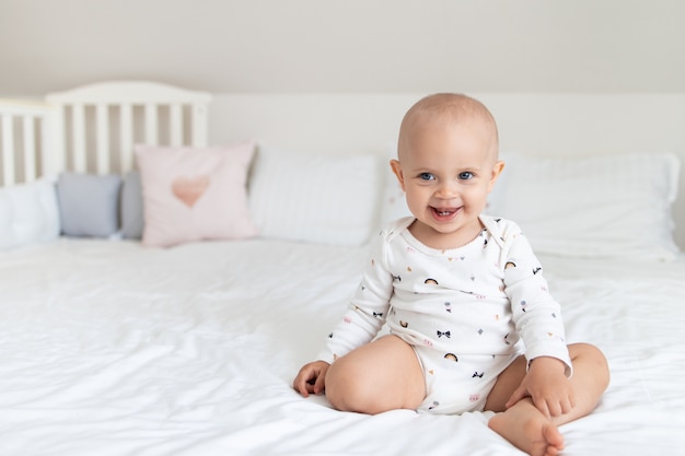 Linda niña en una cama blanca se sienta y sonríe