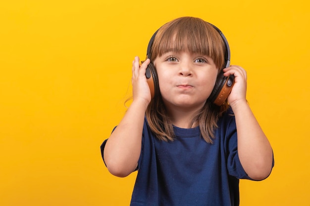 Foto linda niña caucásica con auriculares escuchando música sobre fondo amarillo