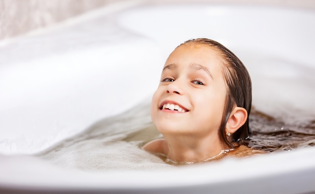 Linda niña caucásica se baña en una bañera con espuma y se divierte durante la cuarentena en casa