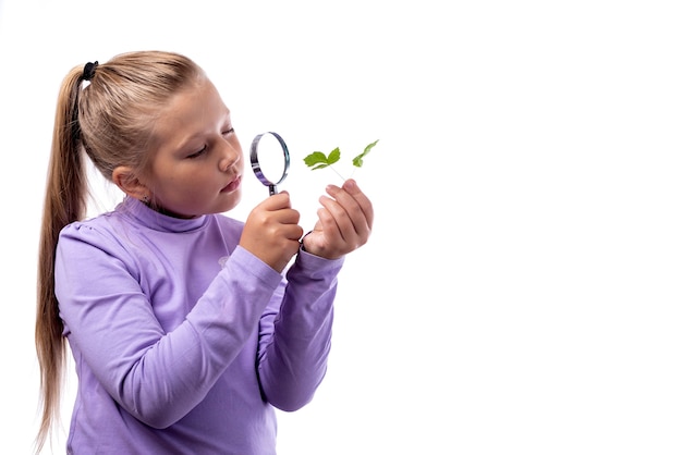 Linda niña caucásica mirando una planta a través de una lupa sobre un fondo blanco.