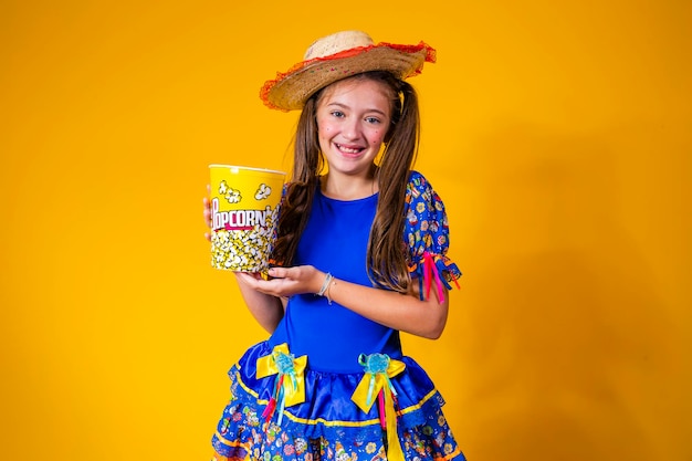 Linda niña caucásica en traje típico de festa junina comiendo palomitas de maíz