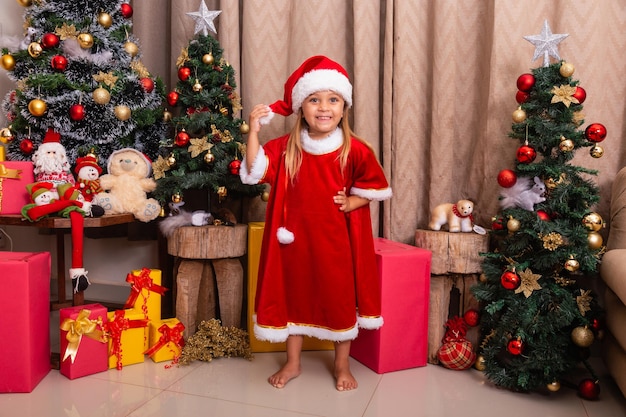 Linda niña caucásica vestida para Navidad en casa. Chica sobre fondo de Navidad vestida de noelete