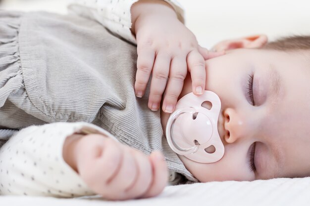 Linda niña con chupete durmiendo sobre colcha blanca