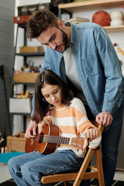 Linda niña colocando cuerdas de guitarra antes de la lección de música con su tutor