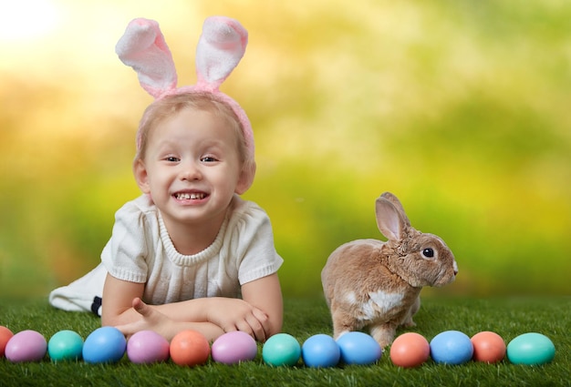 Linda niña con un conejito tiene una pascua en el fondo de hierba verde con espacio de copia