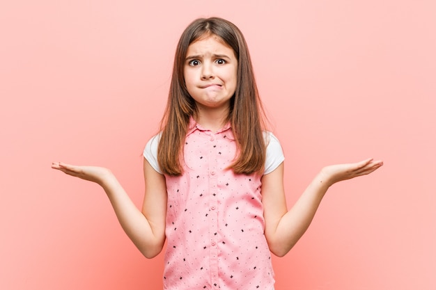 Linda niña confundida y dudosa al levantarle las manos para sostener un espacio de copia.