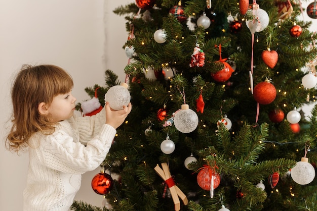 Una linda niña decora el árbol de Navidad en la mañana de Navidad