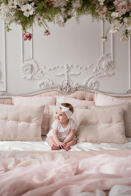 Una linda niña con una diadema blanca y un mono está sentada en una cama en una habitación con un hermoso interior